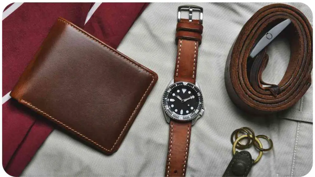 a leather wallet, watch and belt laying on top of a white shirt